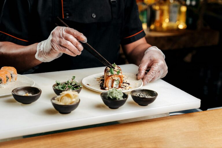 A professional chef artfully organizes sushi with chopsticks, showcasing traditional Japanese cuisine preparation.
