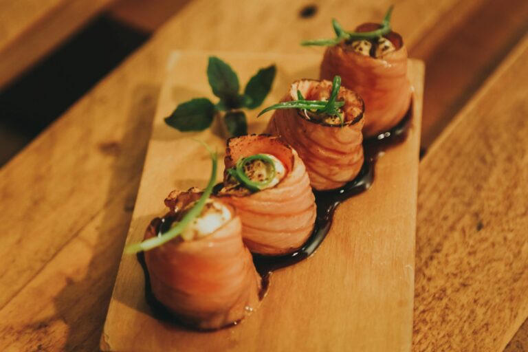 Close-up of salmon sushi rolls garnished with mint leaves served on a wooden plate.