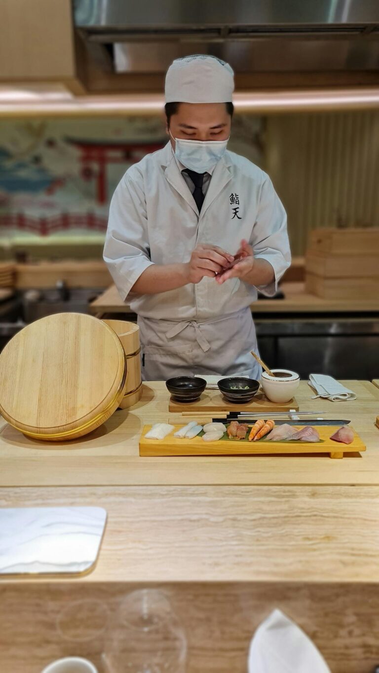 Skilled Japanese chef prepares sushi at restaurant counter, showcasing culinary expertise.